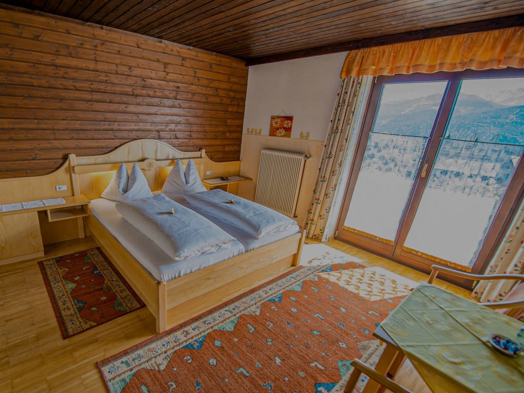 Doppelzimmer mit Holzbetten und Blick durch die Balkontür auf verschneite Berge