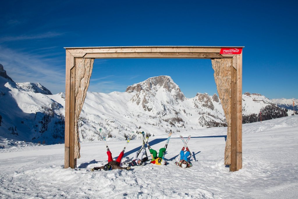 Skifahrer liegen im Schnee unter einem Holzrahmen mit Bergblick am Nassfeld