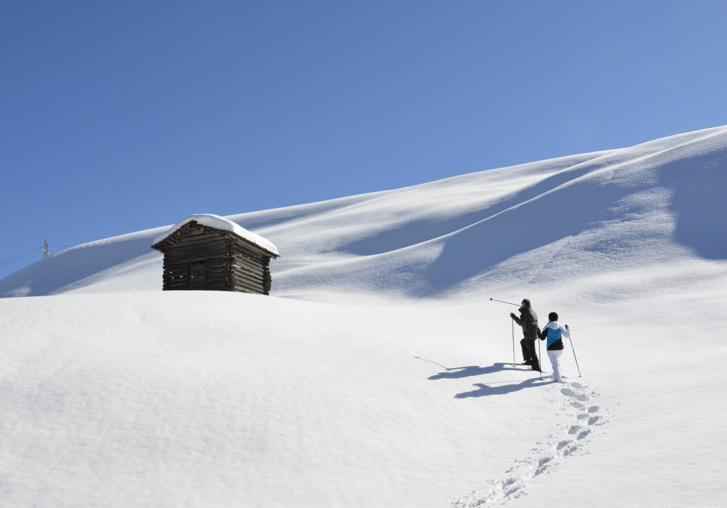Zwei Wanderer ziehen eine Spur im Tiefschnee zu einer Hütte