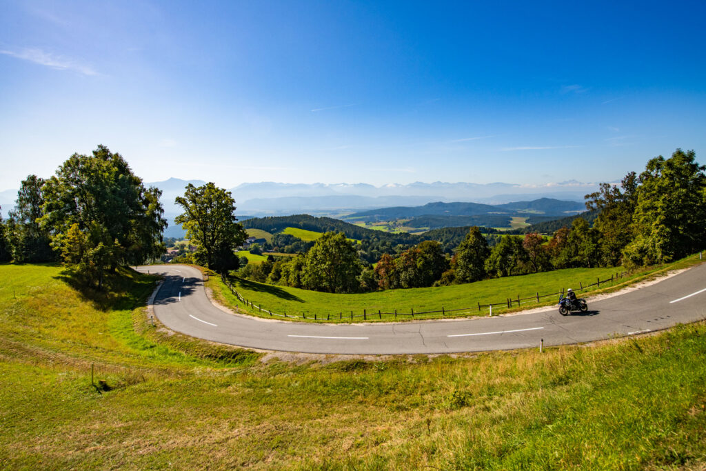 Motorcyclist on a wide bend of a mountain road with a view over meadows, forests and mountains in Carinthia