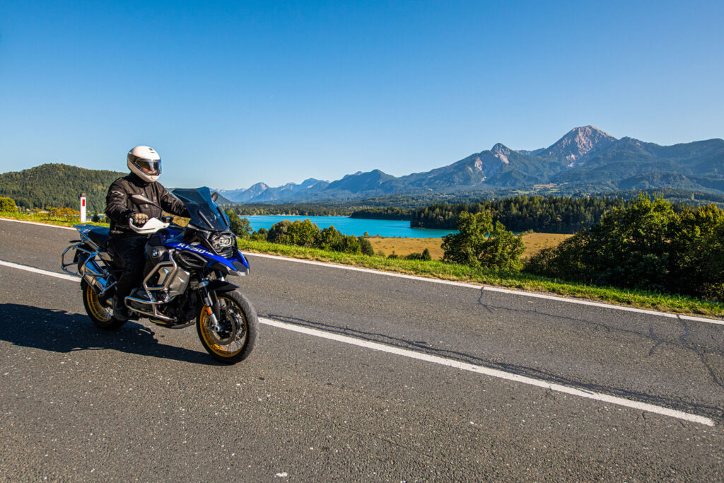 Motociclista su una strada di campagna in Carinzia con vista su un lago e sulle montagne