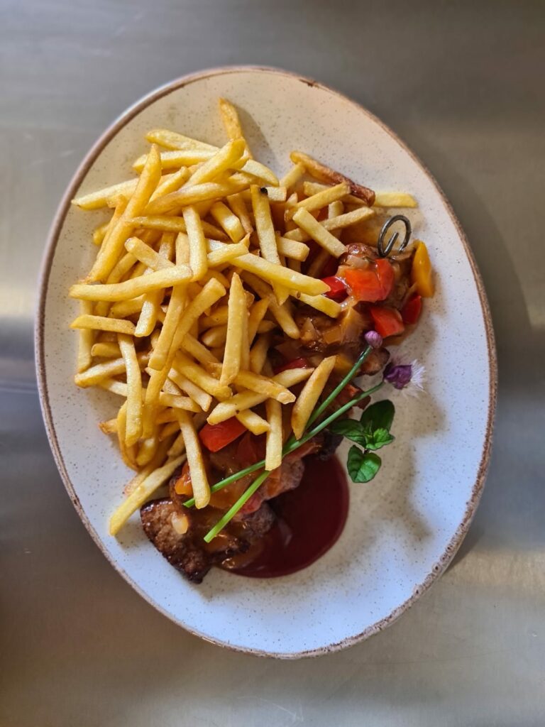 Piatto con carne, patatine fritte e verdure dalla cucina del Berghotel Presslauer