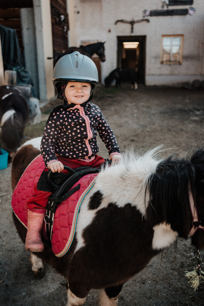 Kleines Kind mit Reithelm auf einem Pony am Hof des Berghotels Presslauer